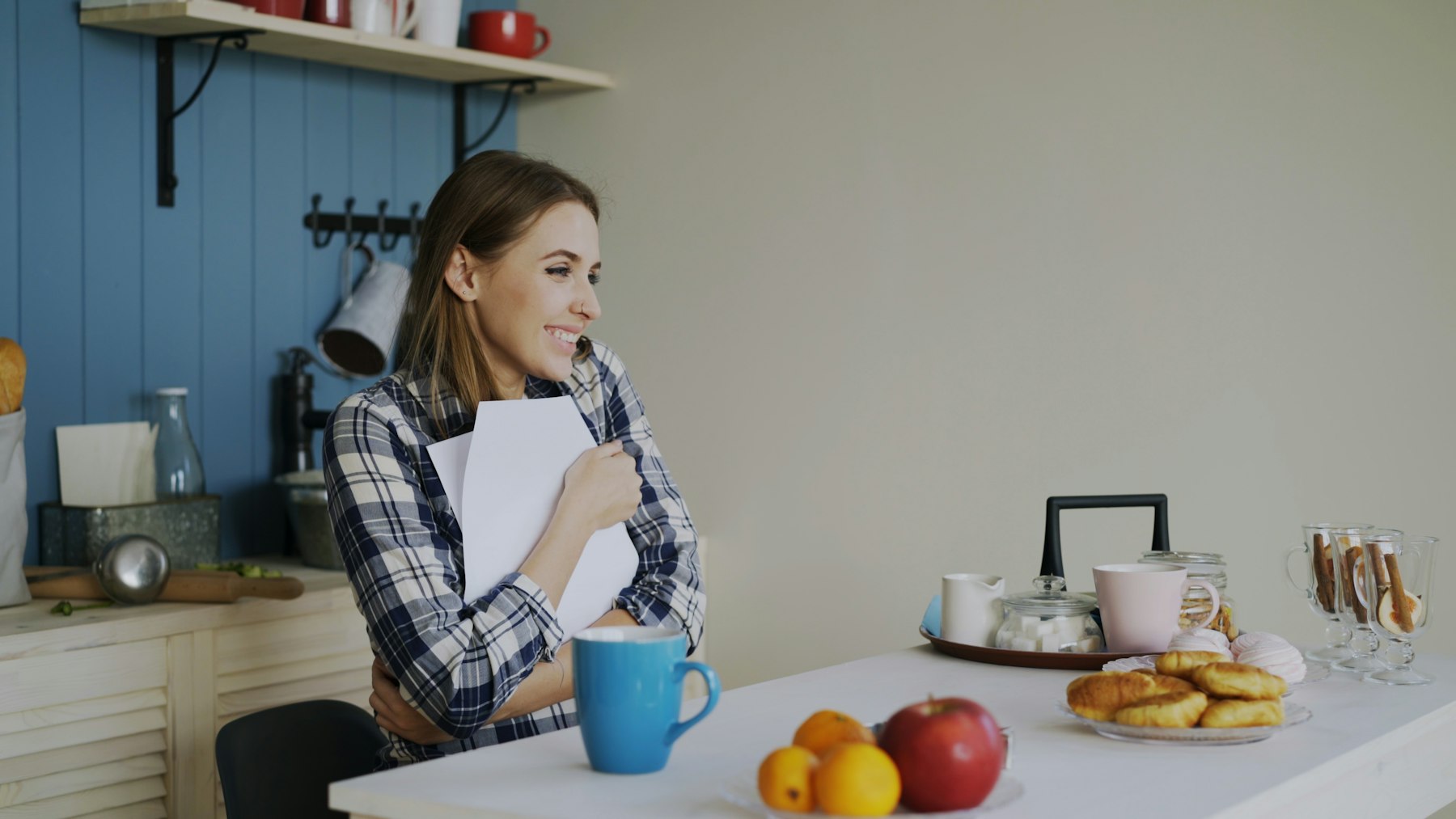 A woman smiling as she reads paperwork at her kitchen table